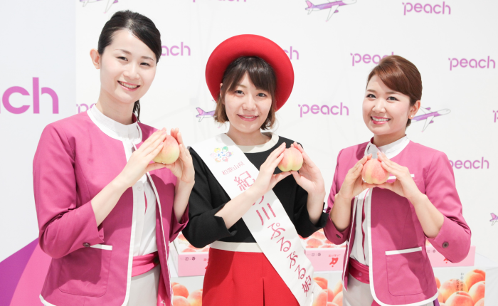 関西空港で行われたLCCピーチ・アビエーションの「和歌山桃キャンペーン」で配布した「紀の川市（JA紀の里）の桃」を持つ客室乗務員とー「紀の川ぷるぷる娘」